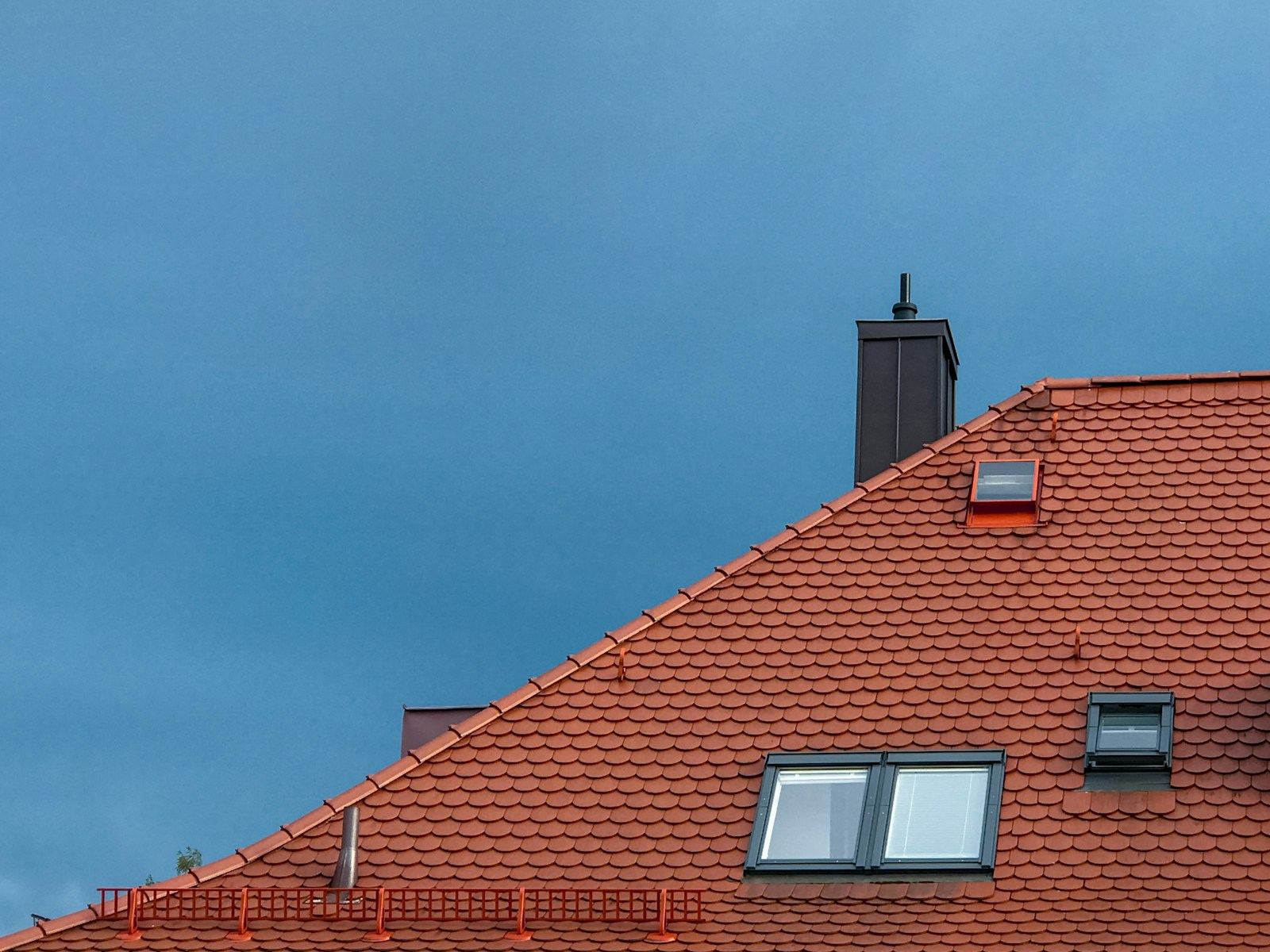 Rood pannendak met een dakraam en een schoorsteen tegen een blauwe lucht